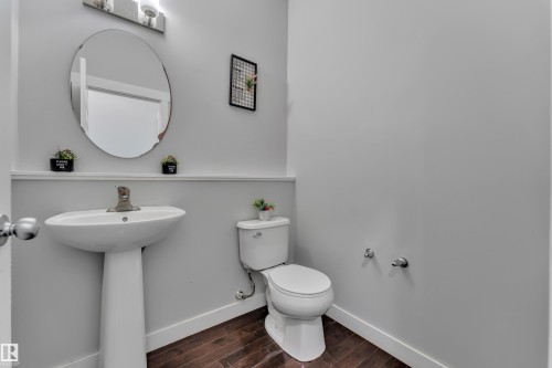 The bathroom features a pedestal sink with a chrome faucet, an oval mirror, and dark wood-look flooring - 1452 30 Street, Edmonton, AB - Indoor Photo Showing Bathroom