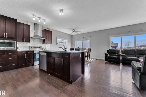 Open concept living area featuring dark hardwood flooring, a kitchen with dark cabinetry, stainless steel appliances, and a white subway tile backsplash, and large windows providing ample natural light - 1452 30 Street, Edmonton, AB - Indoor Photo Showing Kitchen With Upgraded Kitchen