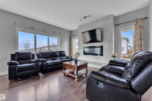 The living room offers large windows providing natural light, dark hardwood floors, and a tiled feature wall with a modern fireplace - 1452 30 Street, Edmonton, AB - Indoor Photo Showing Living Room With Fireplace