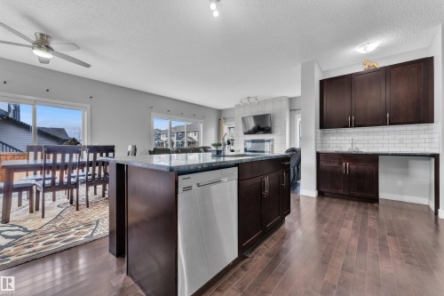 The kitchen features dark wood cabinetry, a central island with a dishwasher, and a sink - 1452 30 Street, Edmonton, AB - Indoor Photo Showing Kitchen
