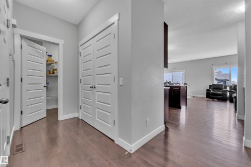 Hallway with hardwood floors, a pantry with shelving, and views into a living area with large windows - 1452 30 Street, Edmonton, AB - Indoor Photo Showing Other Room