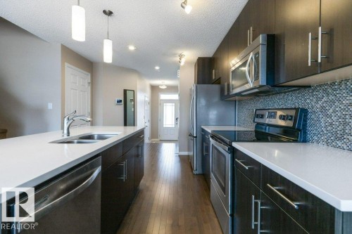 The kitchen features dark wood cabinetry, stainless steel appliances, white countertops, and a mosaic tile backsplash - 3119 Carpenter Landing Landing, Edmonton, AB - Indoor Photo Showing Kitchen With Double Sink With Upgraded Kitchen