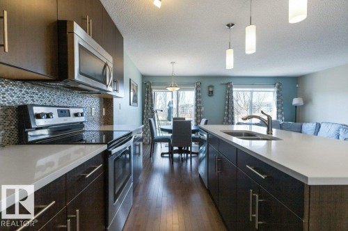 The kitchen features dark wood cabinetry, white countertops, and stainless steel appliances including a microwave and range - 3119 Carpenter Landing Landing, Edmonton, AB - Indoor Photo Showing Kitchen With Double Sink With Upgraded Kitchen