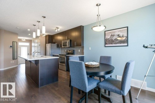 Open concept living space featuring hardwood floors, a kitchen island with seating, dark wood cabinetry, and stainless steel appliances - 3119 Carpenter Landing Landing, Edmonton, AB - Indoor