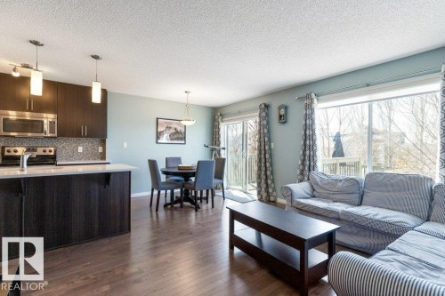 This open-concept living area features hardwood flooring, a kitchen with dark cabinetry and stainless steel appliances, and a dining area with pendant lighting - 3119 Carpenter Landing Landing, Edmonton, AB - Indoor