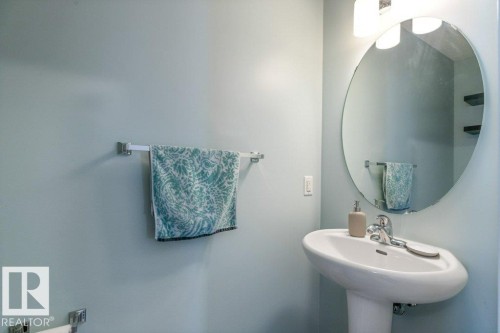 This bathroom features a pedestal sink with a chrome faucet, a circular wall mirror, and light blue walls - 3119 Carpenter Landing Landing, Edmonton, AB - Indoor Photo Showing Bathroom