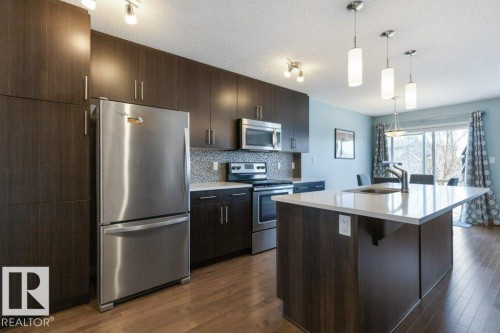 The kitchen features dark wood cabinetry, stainless steel appliances, a white island with an integrated sink, and hardwood floors - 3119 Carpenter Landing Landing, Edmonton, AB - Indoor Photo Showing Kitchen With Stainless Steel Kitchen With Upgraded Kitchen