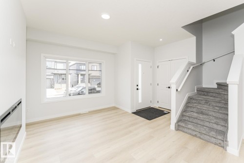 Inviting entry space featuring light-colored flooring, a large window providing natural light, a white entry door, and carpeted stairs with a white railing - 6371 King Wynd, Edmonton, AB - Indoor