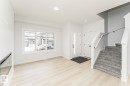 Inviting entry space featuring light-colored flooring, a large window providing natural light, a white entry door, and carpeted stairs with a white railing - 6371 King Wynd, Edmonton, AB  - Indoor 