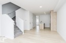 The property features light-toned flooring, a staircase with gray carpeted steps and white railings, and a kitchen island with a black faucet - 6371 King Wynd, Edmonton, AB  - Indoor Photo Showing Other Room 