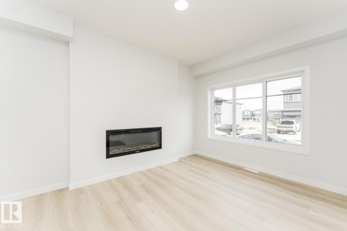 Bright and open room featuring light-toned flooring, an electric fireplace, and a large window providing natural illumination - 6371 King Wynd, Edmonton, AB - Indoor Photo Showing Living Room With Fireplace