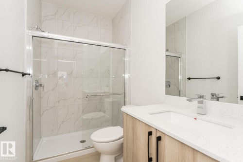 Well-appointed bathroom featuring a shower with a sliding glass door and white tiled walls, a vanity with a white countertop, and a mirror - 6371 King Wynd, Edmonton, AB - Indoor Photo Showing Bathroom