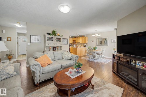 The property features an open-concept living area with dark wood flooring, light grey walls, and ceiling-mounted lighting - 21 1850 Mill Woods Road E, Edmonton, AB - Indoor Photo Showing Living Room