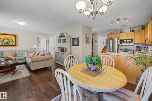 This property features an open-concept living area with dark hardwood flooring, a well-appointed kitchen with light wood cabinetry and stainless steel appliances, and a dining area with a light wood table - 21 1850 Mill Woods Road E, Edmonton, AB - Indoor Photo Showing Dining Room