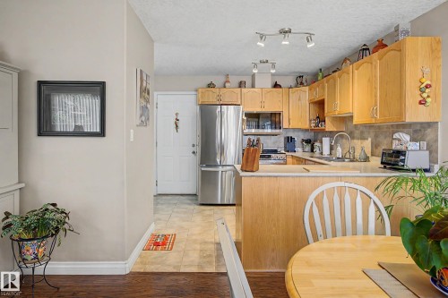 The kitchen features light wood cabinetry, stainless steel appliances, and tile flooring - 21 1850 Mill Woods Road E, Edmonton, AB - Indoor