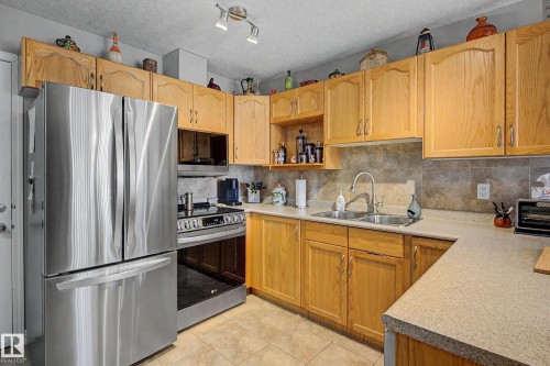 The kitchen features light wood cabinetry, a stainless steel French door refrigerator, and a stainless steel oven - 21 1850 Mill Woods Road E, Edmonton, AB - Indoor Photo Showing Kitchen With Double Sink