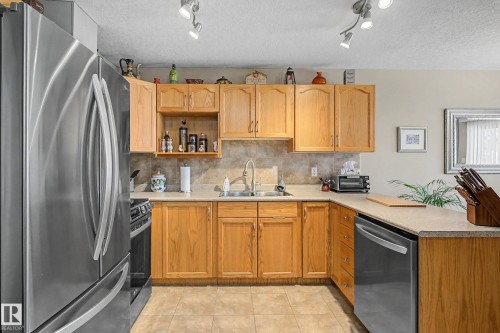 The kitchen features stainless steel appliances, light wood cabinetry, and track lighting - 21 1850 Mill Woods Road E, Edmonton, AB - Indoor Photo Showing Kitchen With Double Sink