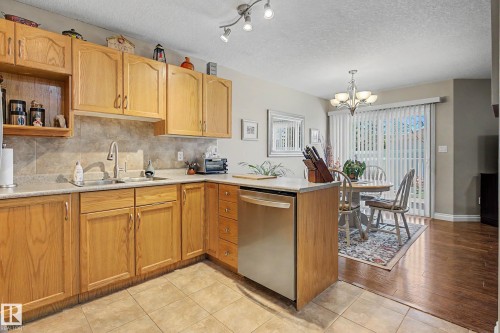The kitchen features wood cabinetry, a stainless steel dishwasher, and tile flooring - 21 1850 Mill Woods Road E, Edmonton, AB - Indoor Photo Showing Kitchen With Double Sink