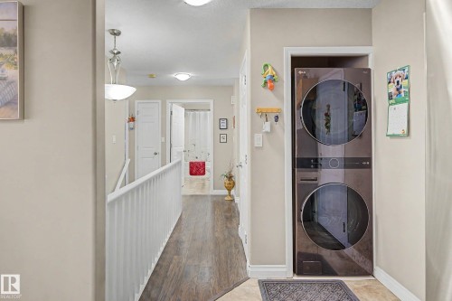 This property features a modern stacked washer and dryer unit, and a hallway with wood-style flooring and light-colored walls - 21 1850 Mill Woods Road E, Edmonton, AB - Indoor Photo Showing Laundry Room