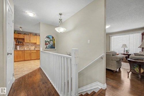 The property features hardwood flooring in the main living areas, a staircase with white railings, and a kitchen with light wood cabinetry and light-colored tiled floors - 21 1850 Mill Woods Road E, Edmonton, AB - Indoor