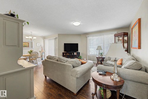The living area features wood-style flooring and a window with blinds - 21 1850 Mill Woods Road E, Edmonton, AB - Indoor Photo Showing Living Room