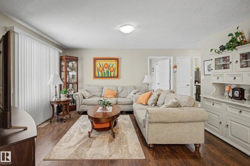 The living room features rich wood flooring, light-colored walls, and a ceiling light fixture - 21 1850 Mill Woods Road E, Edmonton, AB - Indoor Photo Showing Living Room