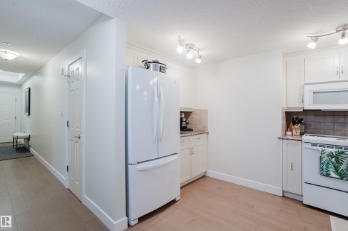 The property features a kitchen with white cabinetry, a white refrigerator, and a white oven with an overhead microwave - 206 10108 125 Street, Edmonton, AB - Indoor Photo Showing Kitchen