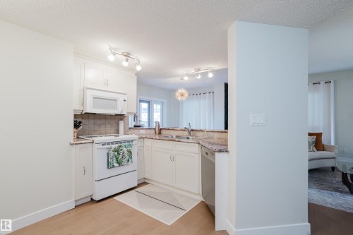 The kitchen features white cabinetry, granite countertops, a tiled backsplash, and stainless steel appliances including a dishwasher and microwave - 206 10108 125 Street, Edmonton, AB - Indoor Photo Showing Kitchen
