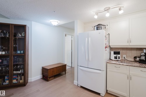 The kitchen features white cabinetry, a white refrigerator, a tiled backsplash, and a countertop with visible veining - 206 10108 125 Street, Edmonton, AB - Indoor Photo Showing Kitchen