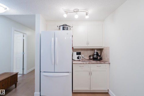 The kitchen features white cabinetry, a white refrigerator, and granite countertops with a tiled backsplash - 206 10108 125 Street, Edmonton, AB - Indoor