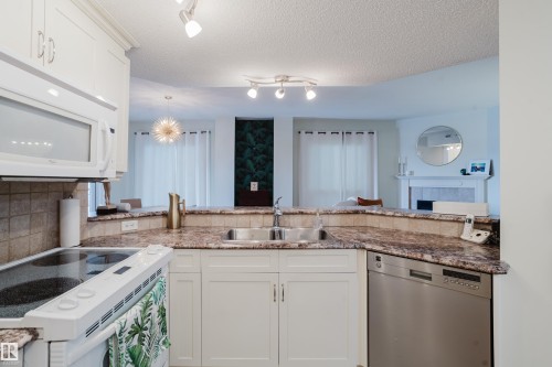 The kitchen features white cabinetry, a double basin stainless steel sink, a stainless steel dishwasher, and a built-in microwave - 206 10108 125 Street, Edmonton, AB - Indoor Photo Showing Kitchen With Double Sink