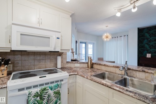 The kitchen features white cabinetry, a white microwave, and a white electric stove - 206 10108 125 Street, Edmonton, AB - Indoor Photo Showing Kitchen With Double Sink