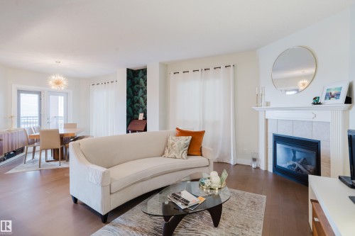 The living area features hardwood floors, a fireplace with a mantel, and a dining area with a modern chandelier - 206 10108 125 Street, Edmonton, AB - Indoor Photo Showing Living Room With Fireplace