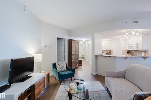 The property features hardwood floors and an open concept layout, with a partial view of the kitchen showcasing white cabinetry, a microwave, and track lighting - 206 10108 125 Street, Edmonton, AB - Indoor Photo Showing Living Room