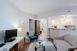 The property features hardwood floors and an open concept layout, with a partial view of the kitchen showcasing white cabinetry, a microwave, and track lighting - 