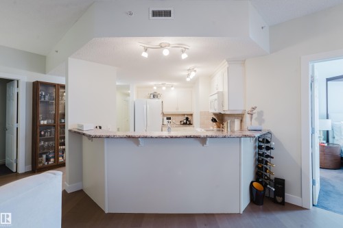 The kitchen features white cabinetry, a refrigerator, a microwave, and a breakfast bar with a granite countertop - 206 10108 125 Street, Edmonton, AB - Indoor Photo Showing Kitchen