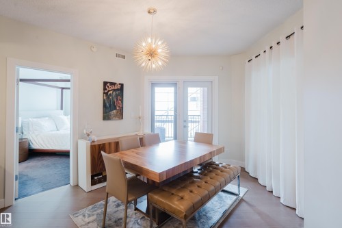 Dining area featuring hardwood floors, a contemporary chandelier, and direct access to an outdoor balcony through glass doors - 206 10108 125 Street, Edmonton, AB - Indoor Photo Showing Dining Room