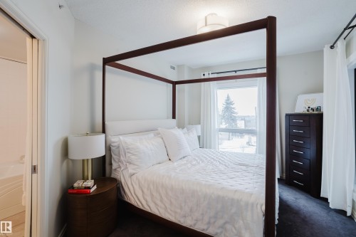 This bedroom features a large window with white curtains, providing ample natural light - 206 10108 125 Street, Edmonton, AB - Indoor Photo Showing Bedroom