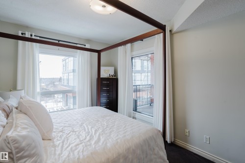 This bedroom features two windows, one of which includes a balcony view, and a ceiling light fixture - 206 10108 125 Street, Edmonton, AB - Indoor Photo Showing Bedroom