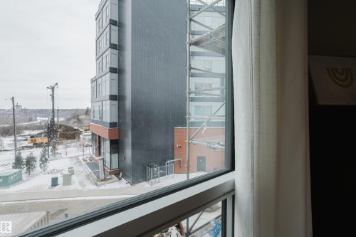 View of the surrounding buildings and snow-covered ground from a window with a white curtain - 206 10108 125 Street, Edmonton, AB -  Photo Showing Other Room