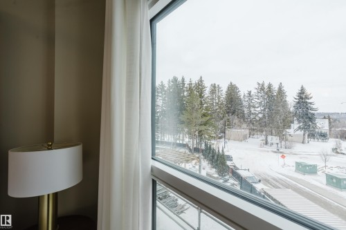 Expansive window offering views of the surrounding natural landscape, including mature trees and a snow-covered street - 206 10108 125 Street, Edmonton, AB - Indoor