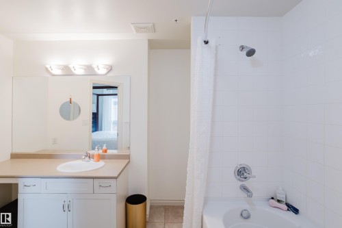 The bathroom features a vanity with an integrated sink, a large mirror, and a three-light fixture - 206 10108 125 Street, Edmonton, AB - Indoor Photo Showing Bathroom