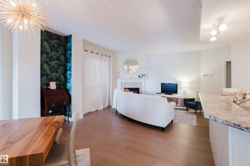 The open-concept living space features light wood flooring, a fireplace with a white mantel, and track lighting - 206 10108 125 Street, Edmonton, AB - Indoor