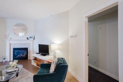 The living area features hardwood flooring, a fireplace with a white mantel, and a rounded mirror - 206 10108 125 Street, Edmonton, AB - Indoor Photo Showing Living Room With Fireplace