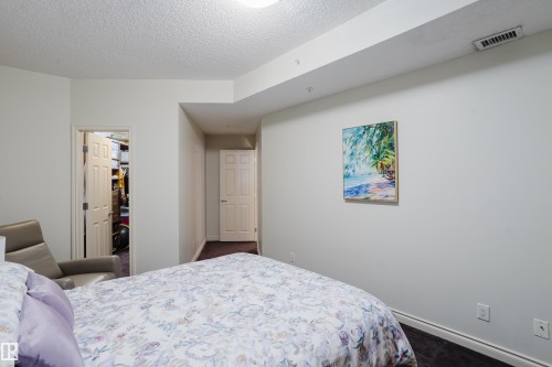 This room features a neutral color palette, a textured ceiling, and a doorway leading to a walk-in closet - 206 10108 125 Street, Edmonton, AB - Indoor Photo Showing Bedroom