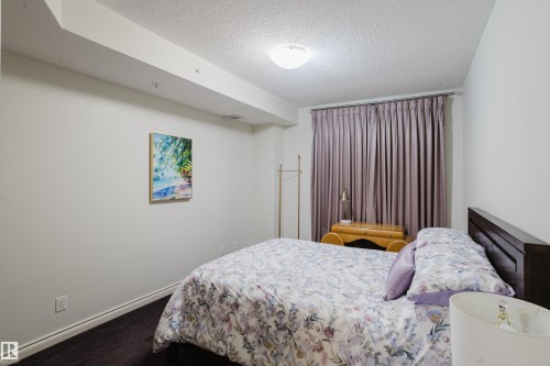 This bedroom features dark flooring, light-colored walls, and a ceiling light fixture - 206 10108 125 Street, Edmonton, AB - Indoor Photo Showing Bedroom