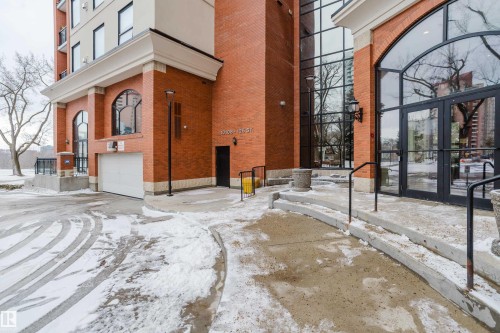 The property features a brick exterior with arched windows, a large glass entrance, and a garage door - 206 10108 125 Street, Edmonton, AB - Outdoor