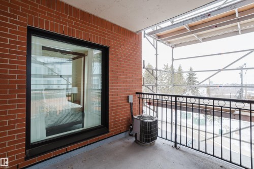 This balcony features a brick exterior wall, a large window, and a black metal railing - 206 10108 125 Street, Edmonton, AB - Outdoor With Exterior