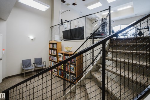 This property features a carpeted staircase with a metal railing and a wall-mounted light fixture - 206 10108 125 Street, Edmonton, AB - Indoor Photo Showing Other Room