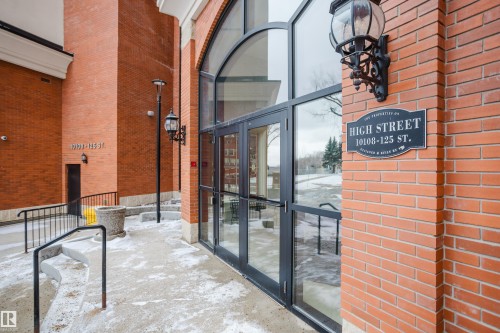 The property features a brick exterior with large arched windows and a decorative outdoor wall lantern - 206 10108 125 Street, Edmonton, AB - Outdoor With Exterior